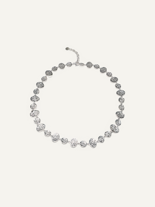 A silver-toned beaded necklace with textured, organic-shaped beads and a matching extender clasp, displayed on a light cream background.