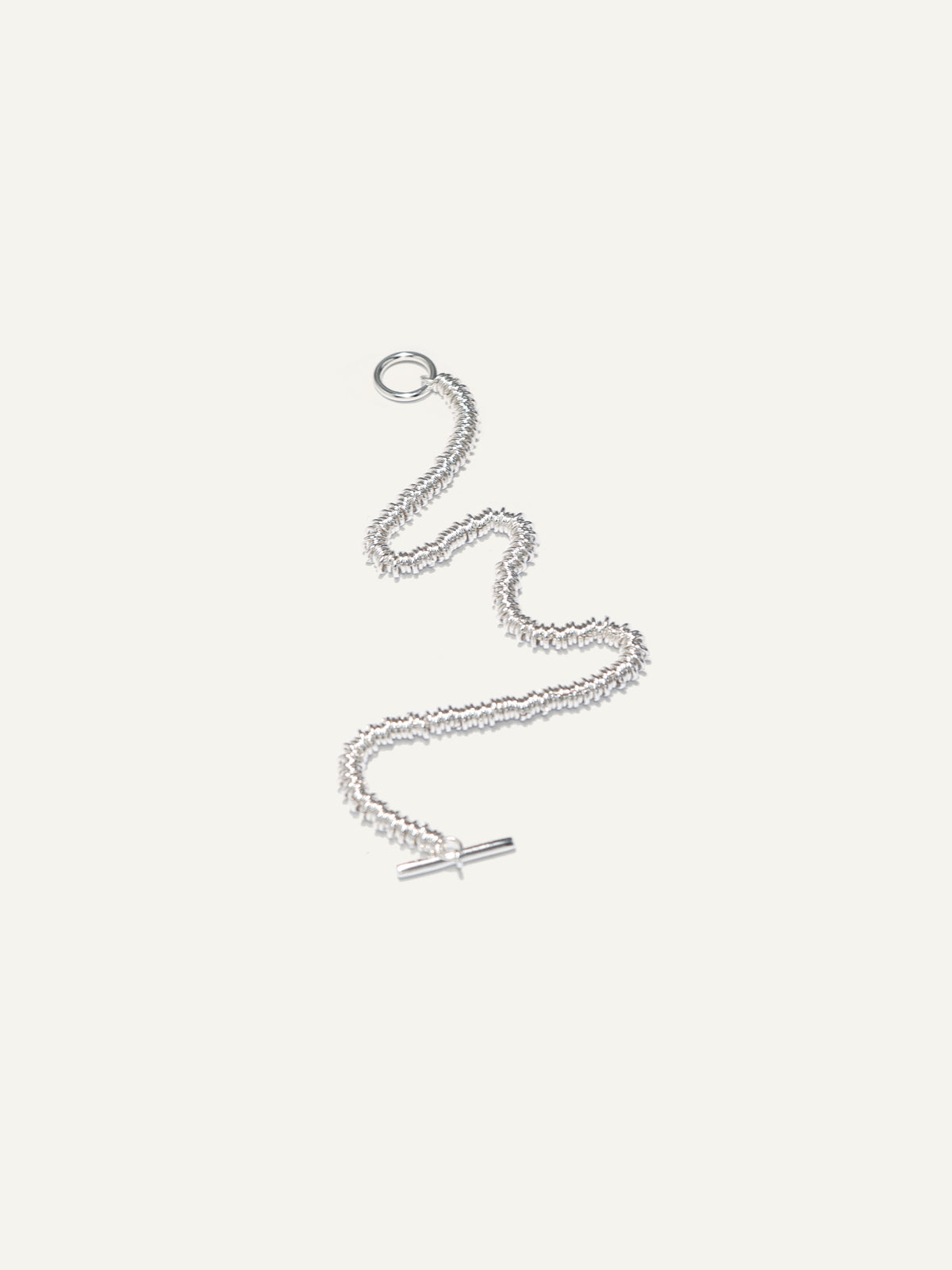 A silver chain necklace with a distinctive wavy, textured link design and a small horizontal bar clasp, displayed on a solid off-white background.